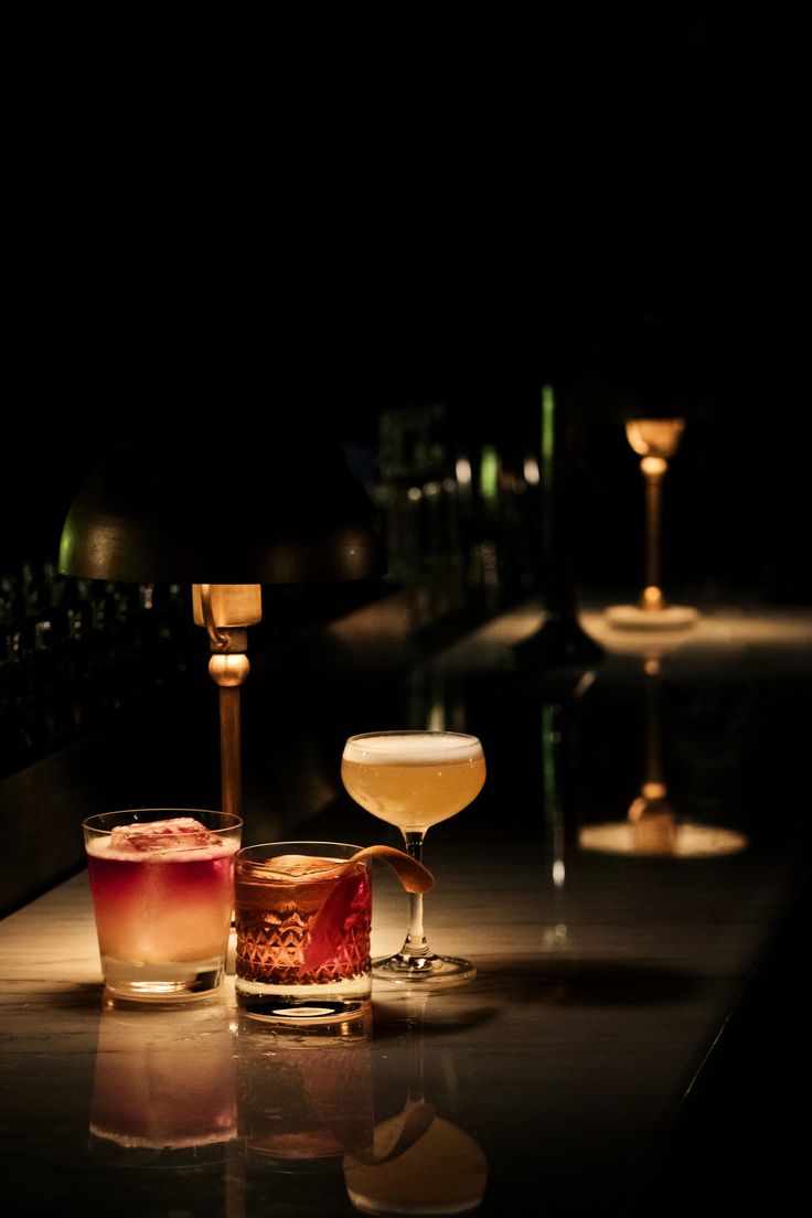 three different types of drinks sitting on a bar with one light on and the other half empty