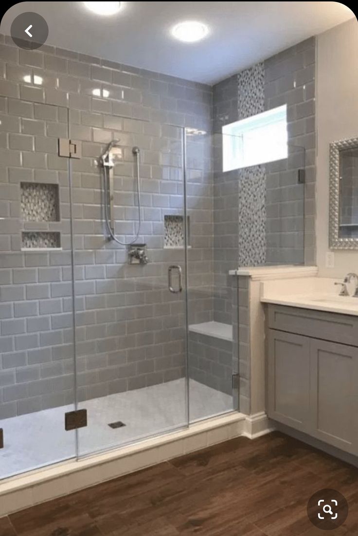 a bathroom with a walk in shower next to a white sink and wooden flooring