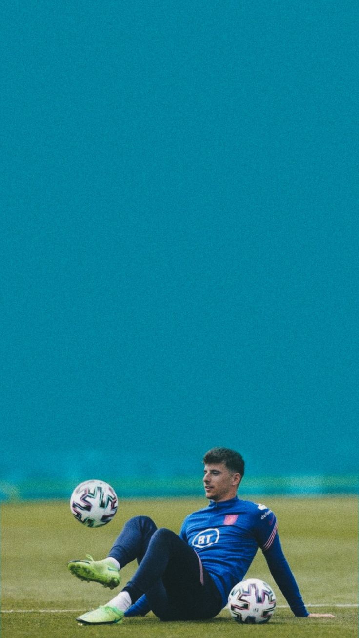 a man sitting on the ground with two soccer balls in his hands and one foot up