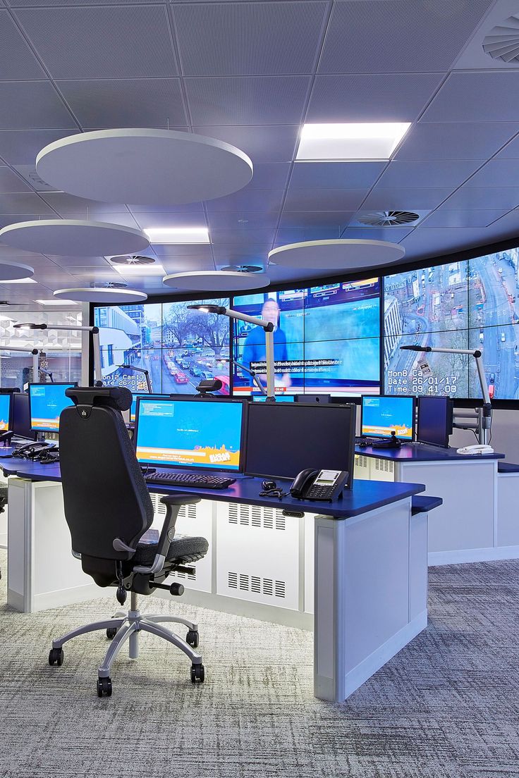 an office with multiple monitors and desks in front of the wall mounted televisions