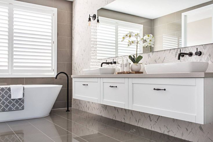 a white bath tub sitting next to a sink in a bathroom under a window with shutters