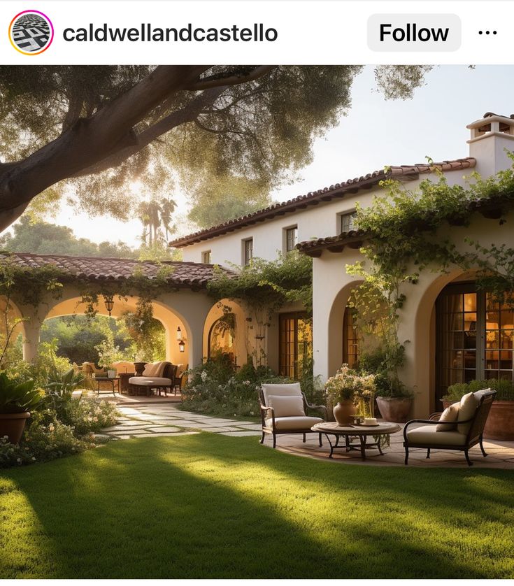 an outdoor patio with chairs and tables in the grass near a house that is surrounded by greenery