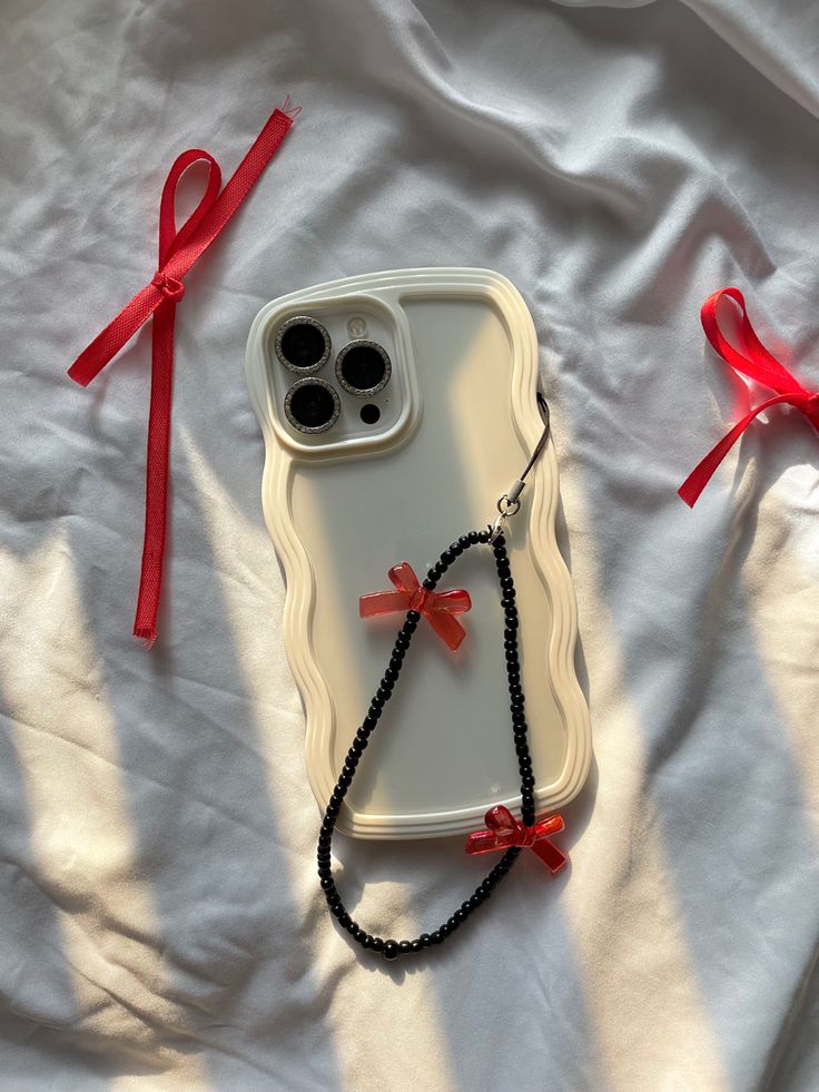 an iphone case with a red ribbon on it and two black beads attached to the back