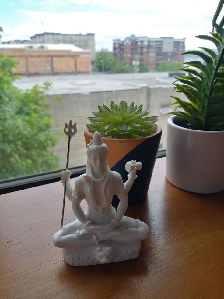 a small statue sitting on top of a wooden table next to a potted plant