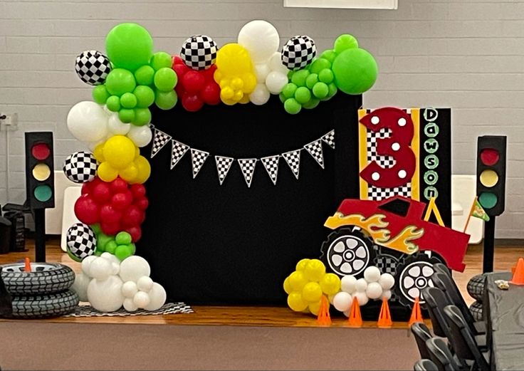 a birthday decoration with balloons and cars on the table in front of it is an arch