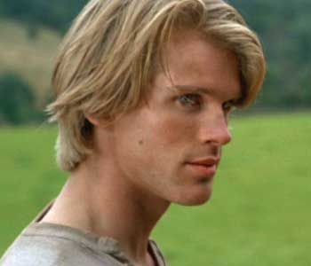 a close up of a person in a field with green grass and trees behind him