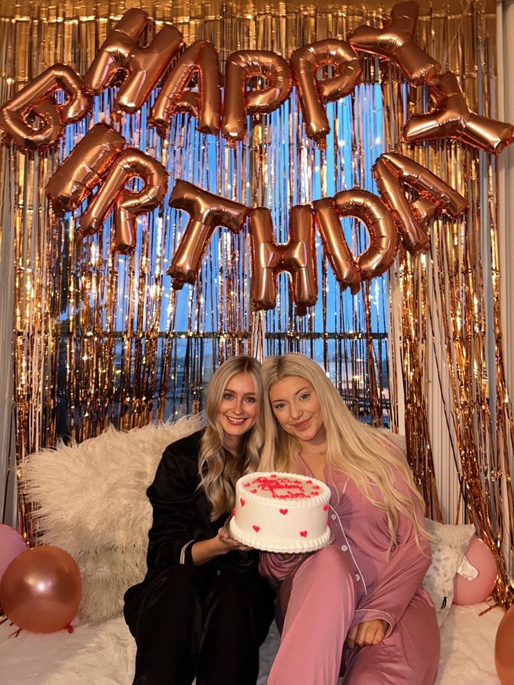 two women sitting next to each other in front of a birthday sign and balloon arch