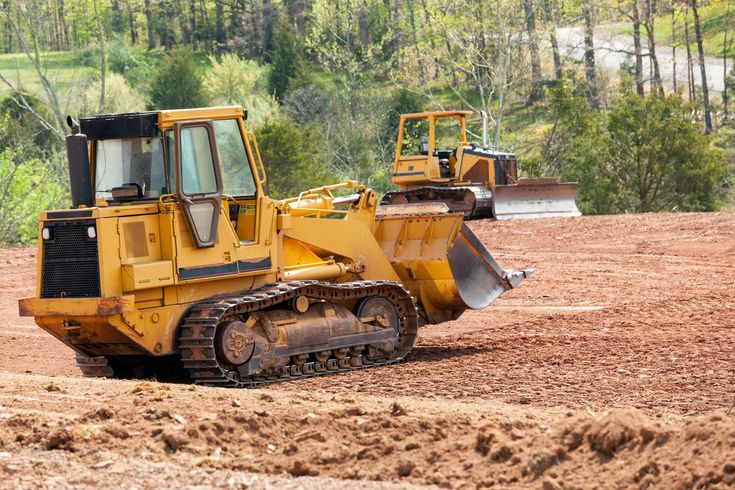 two yellow bulldozers are parked in the dirt