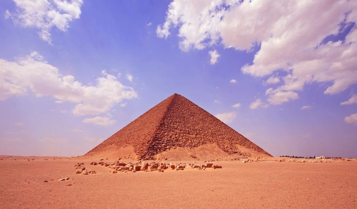 a large pyramid in the desert under a blue sky with some white clouds above it