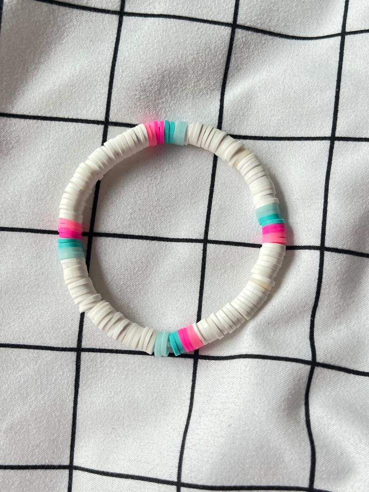 a white bracelet with pink, blue and green beads sitting on top of a bed