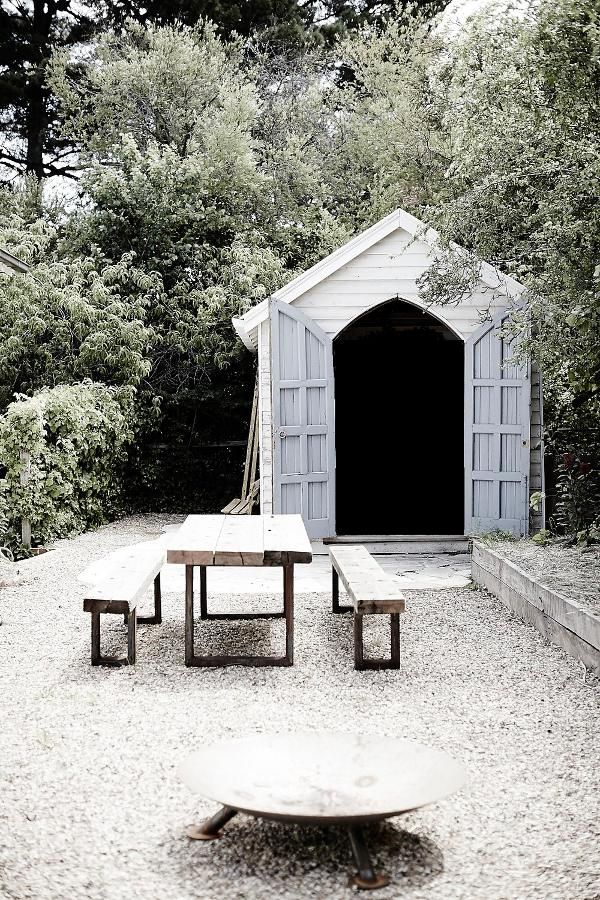 a picnic table and benches in front of a dog house with trees around it on gravel ground