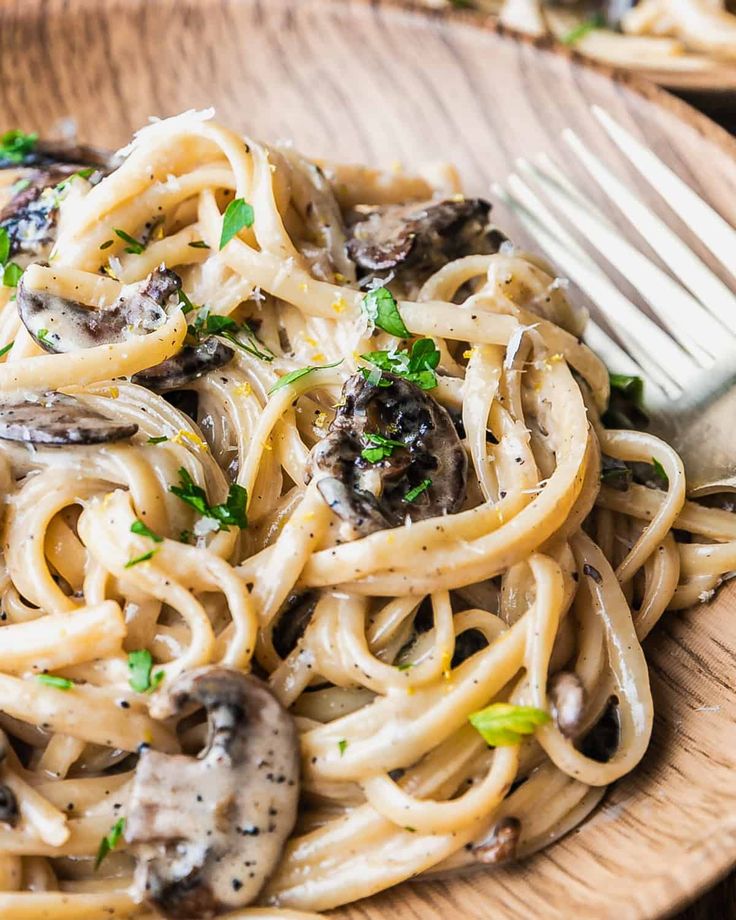 a plate of pasta with mushrooms and parsley on the side next to a fork