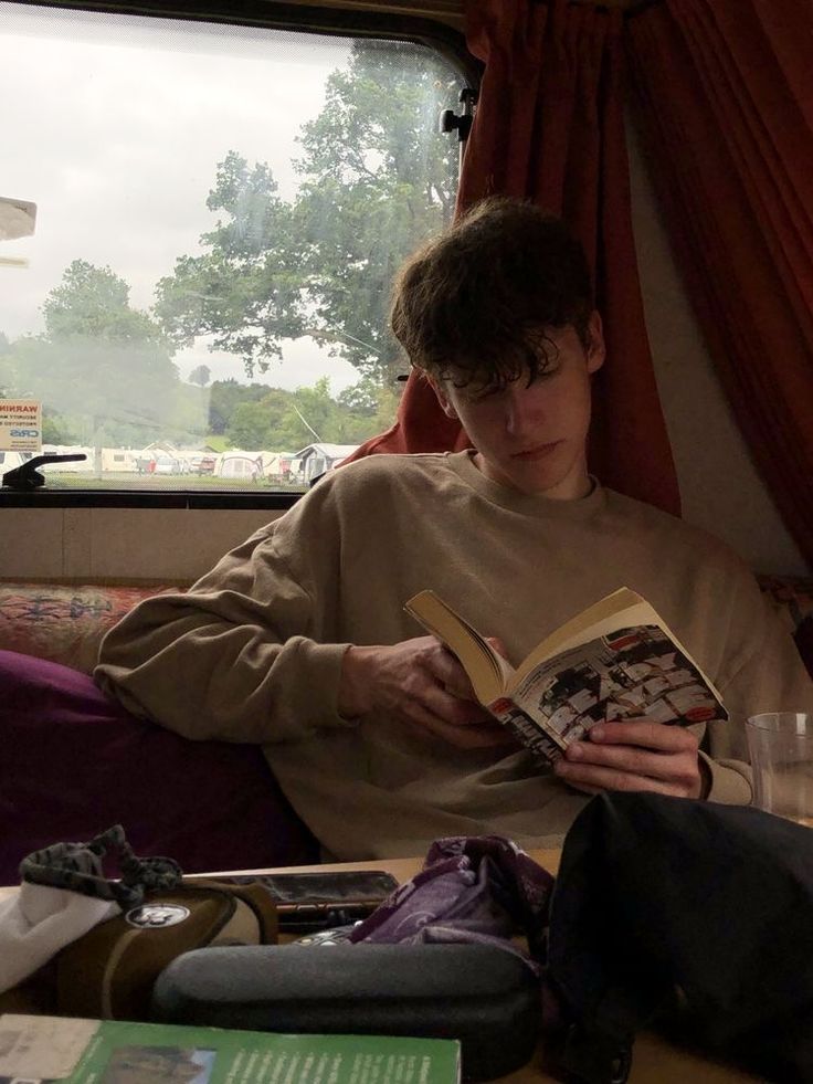 a young man reading a book while sitting on a couch in front of a window