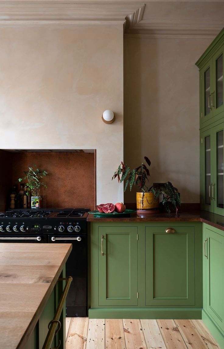 a kitchen with green cabinets and wood flooring next to a stove top oven on a wooden counter