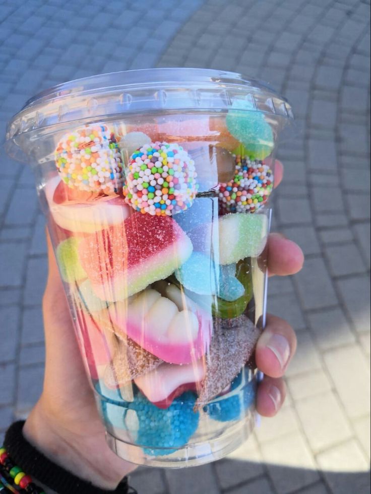 a person holding up a plastic cup filled with lots of candies and sprinkles