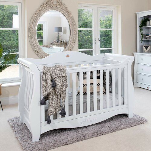 a white baby crib in a room with windows and rugs on the floor