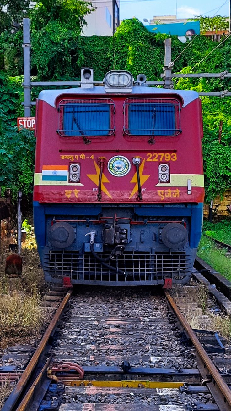 a red and blue train traveling down train tracks next to some trees in the background