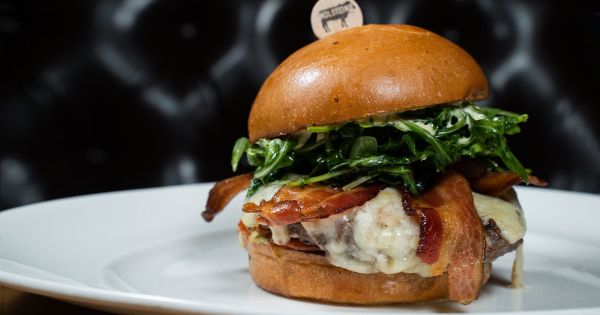 a close up of a sandwich on a plate with meat and greens in the middle