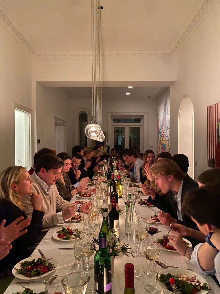 a group of people sitting at a long table with food and wine in front of them