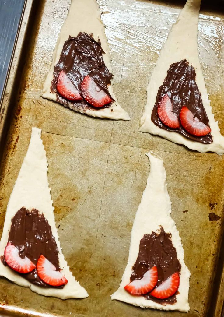 four pastries with chocolate and strawberries on them in the shape of horns, sitting on a baking sheet