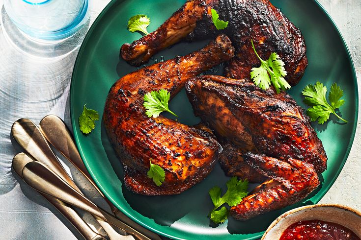 grilled chicken legs on a plate with garnishes and silverware next to water