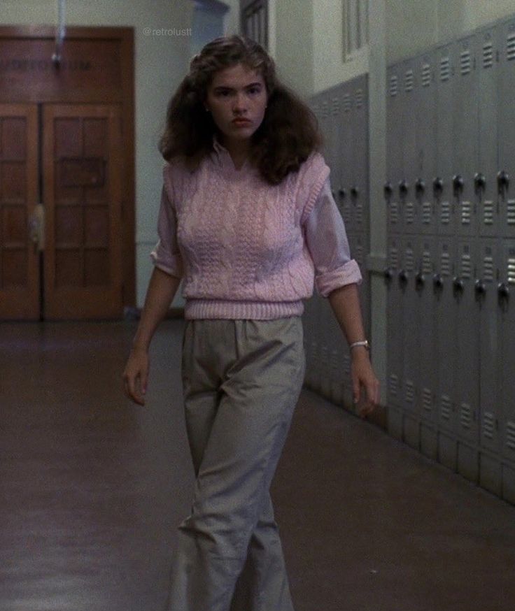 a woman walking down a hallway with lockers in the background