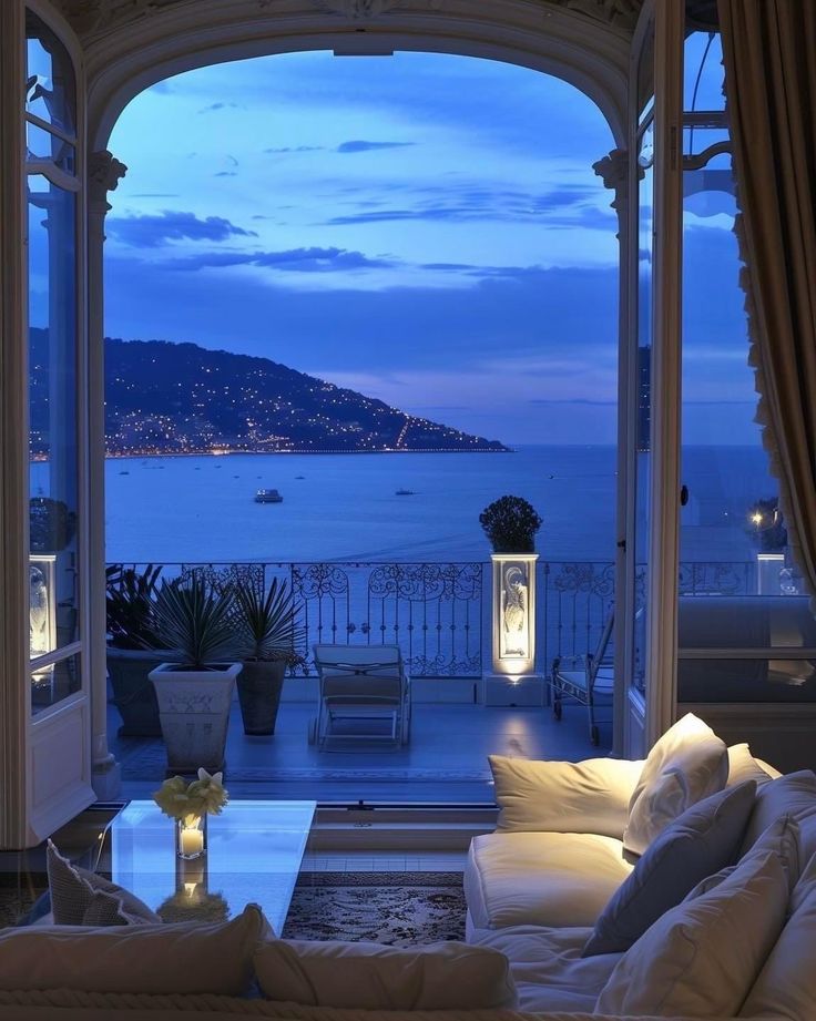 a living room filled with furniture next to a large window overlooking the ocean at night