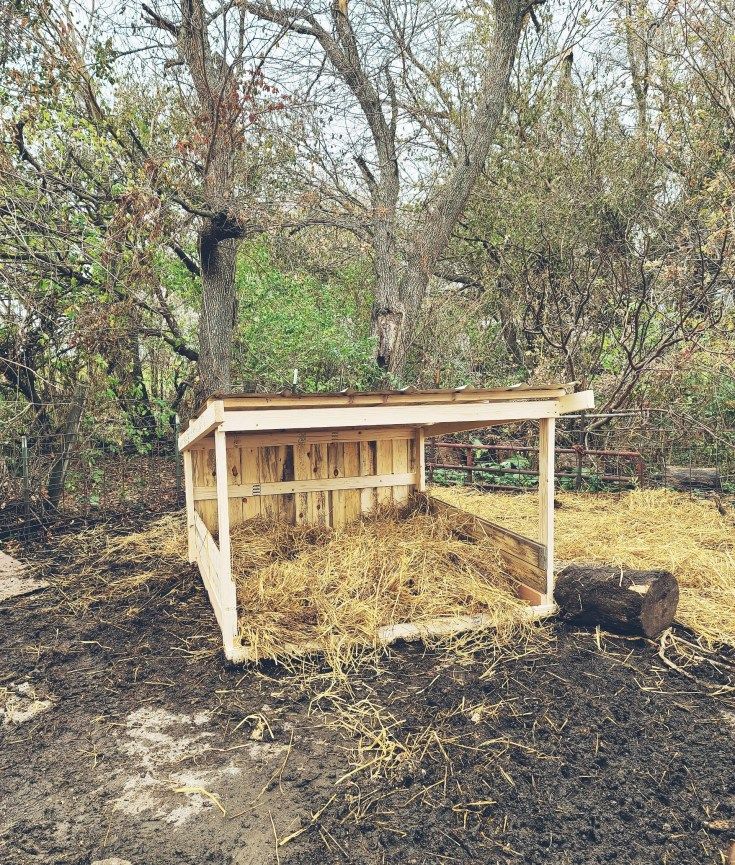 an outhouse in the middle of a field with hay and trees around it,