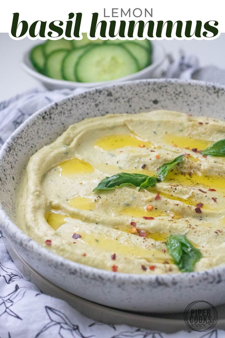 a bowl of hummus with some sliced cucumbers in the background