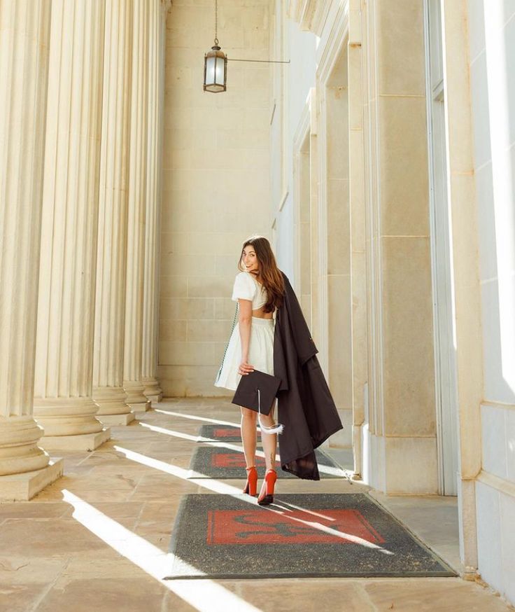 a woman is walking down the street in front of some pillars and columns with her coat over her shoulders