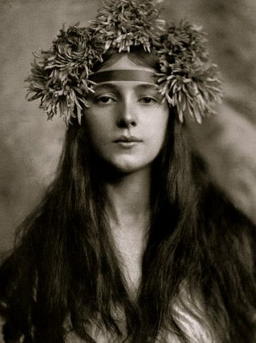 an old photo of a woman with long hair wearing a headdress and flowers in her hair