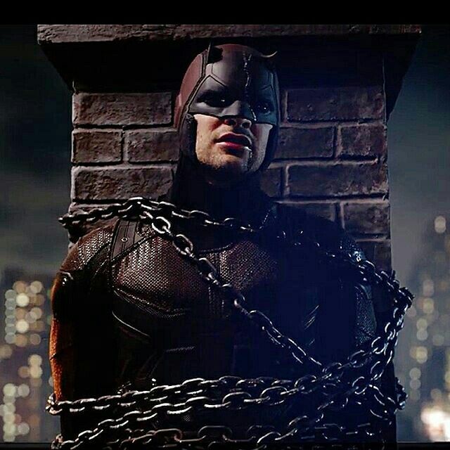 a man in a batman costume standing next to a brick wall with chains on it