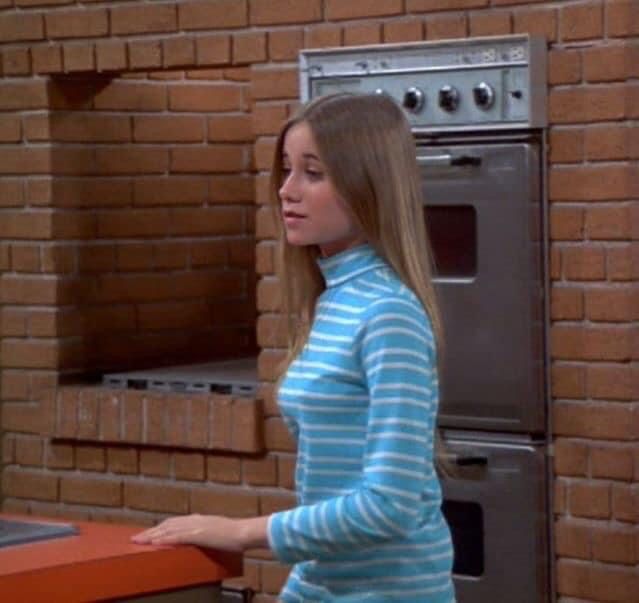 a woman standing in front of a brick wall next to an oven and counter top