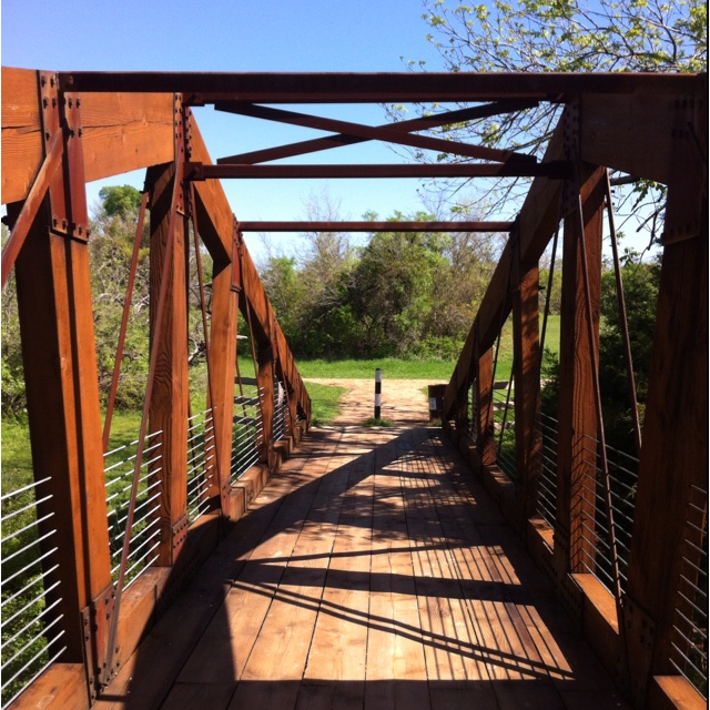 a wooden bridge with metal railings and trees in the background on a sunny day