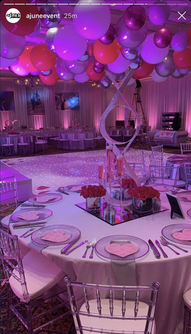 a table set up for a party with pink and white balloons hanging from the ceiling