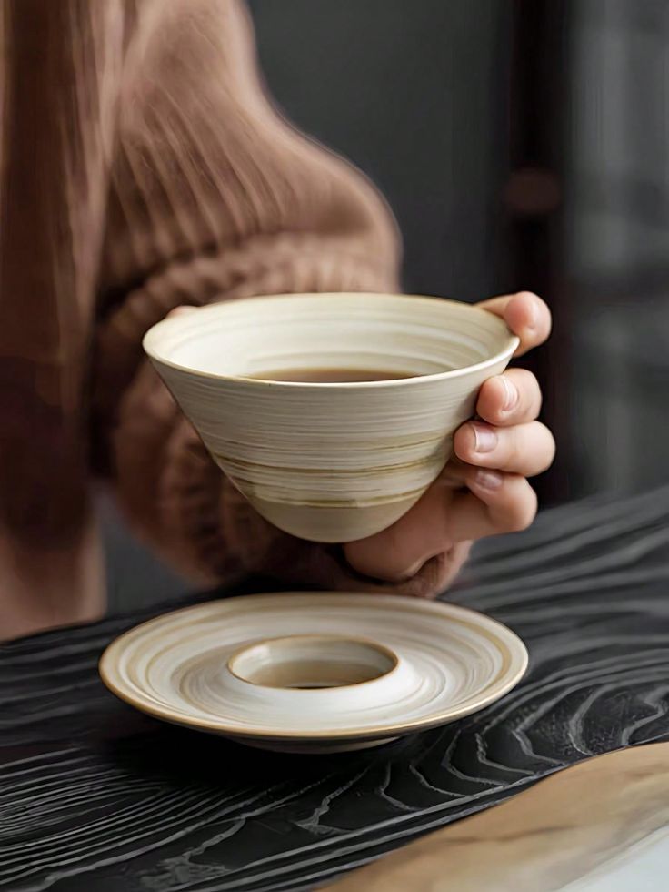 a person holding a white bowl on top of a wooden table next to a plate