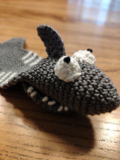 a crocheted toy alligator laying on top of a wooden table next to a pair of gloves