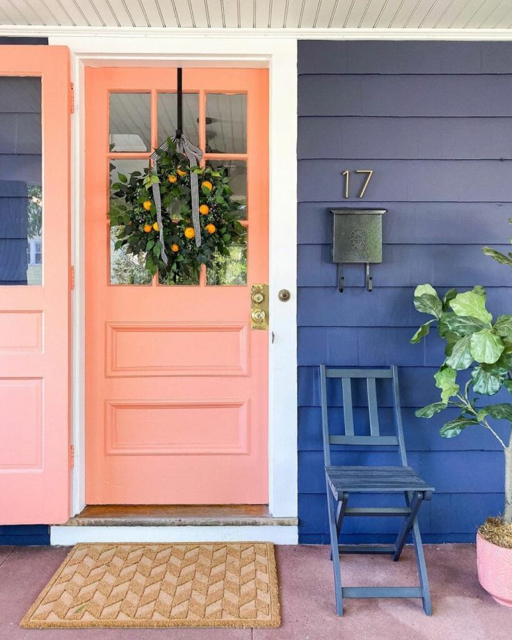 an orange front door with two chairs and a potted plant