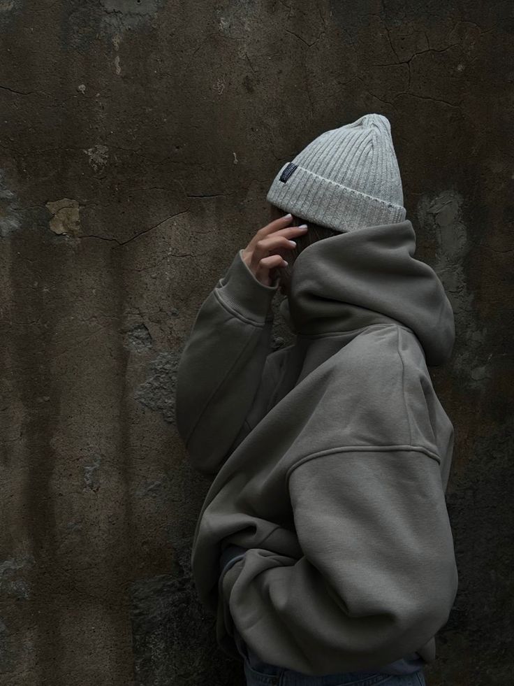 a person wearing a gray hoodie with a hat on their head and covering his face