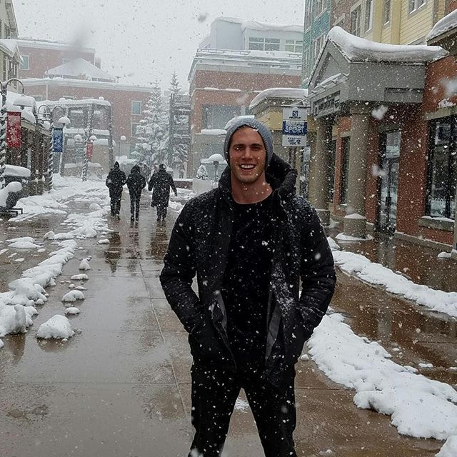 a man standing in the middle of a snow covered street with people walking down it