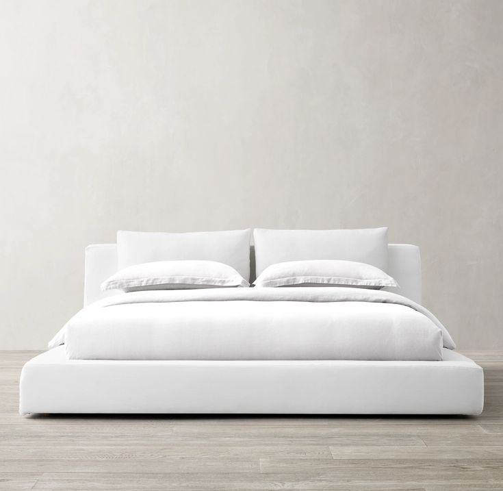 a bed with white sheets and pillows on top of it in a room that has wood floors