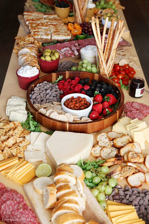 an assortment of cheeses, fruits and crackers on a table with other snacks