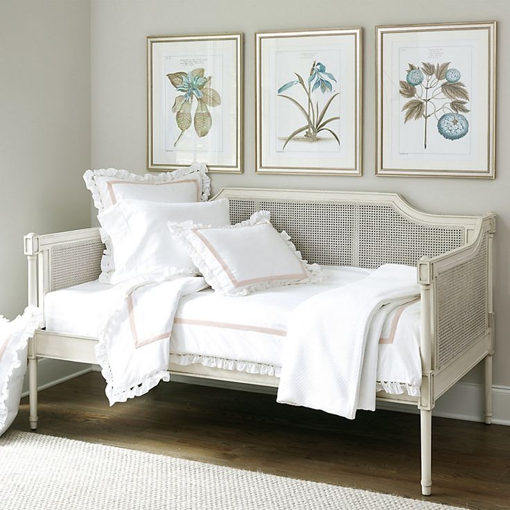 a white day bed sitting in a bedroom next to two framed pictures on the wall