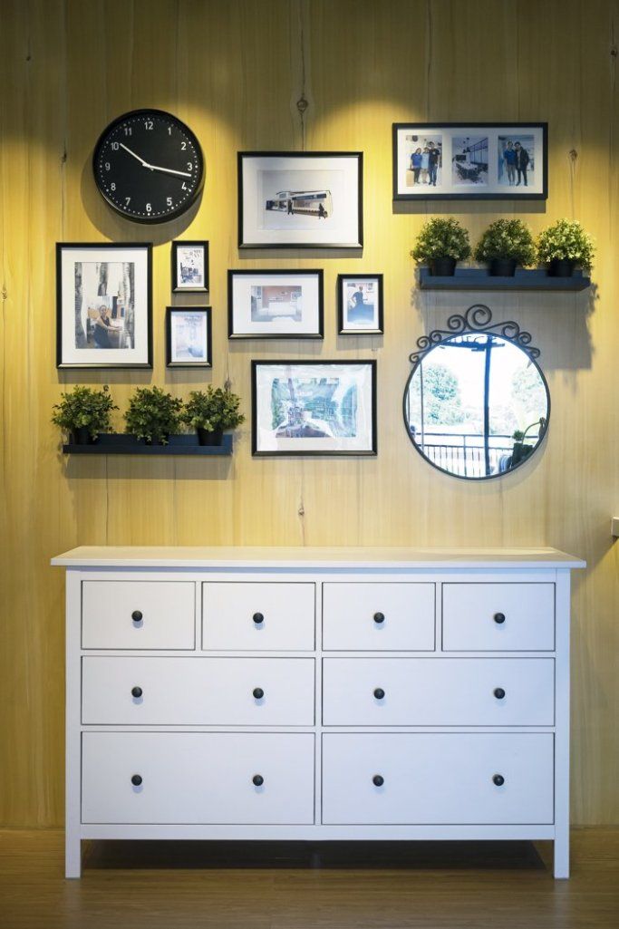 a white dresser sitting in front of a wall filled with pictures and framed photos next to a clock