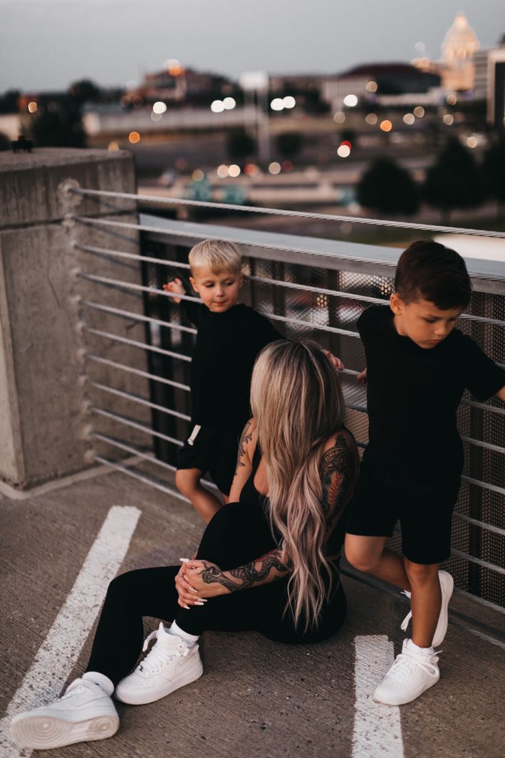 two young boys and a woman sitting on top of a bridge looking at the camera