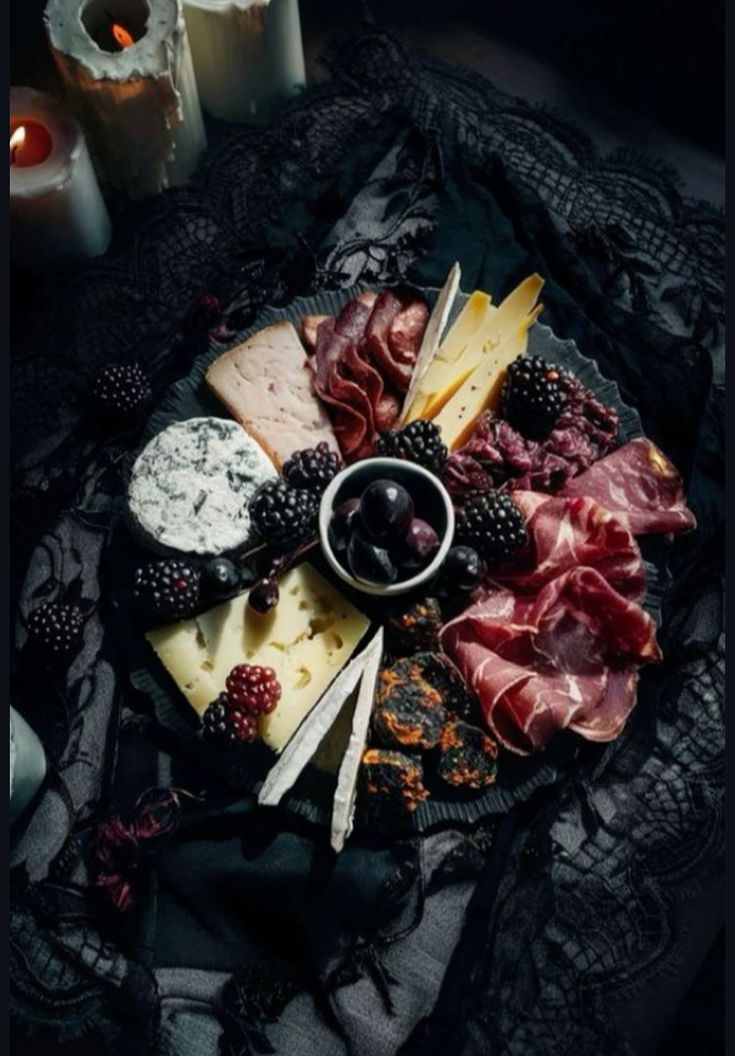 an assortment of cheeses and meats on a platter with candles in the background