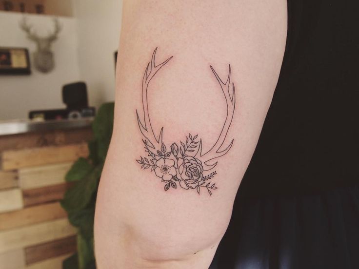 a woman's arm with a tattoo on it that has flowers and antlers in the middle