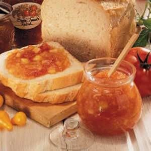 bread, jam and tomatoes sit on a table next to jars of jelly or honey