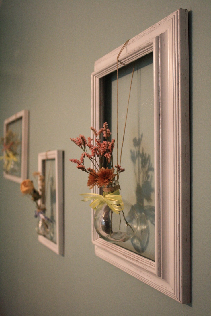 three framed pictures hang on the wall with dried flowers in vases hanging from them