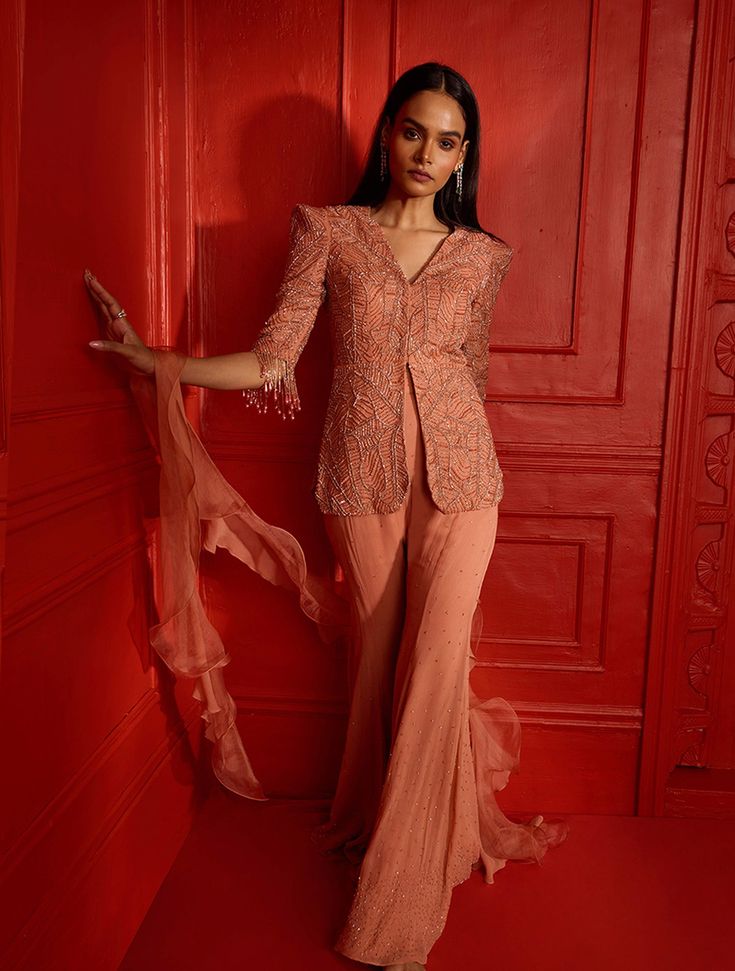 Dusty peach power shoulder crop jacket with cropped sleeves heavily hand embellished with our self geometric leaf design. The jacket features glass beaded tassels at the sleeve hems. Paired with a flowy georgette pant featuring hand embellished scatters & a ruffle dupatta.From Shloka Khialani's Afterglow CollectionDELIVERY TIMEPlease allow 8-12 weeks for your outfit to arrive.FABRIC DETAILSGeorgette, Net, OrganzaSpot Dry Clean Only. Elegant Peach Sets For Reception, Elegant Peach Reception Set, Spring Evening Hand Embellished Sets, Spring Evening Hand-embellished Sets, Elegant Tassel Sets For Reception, Elegant Embellished Peach Sets, Elegant Peach Embellished Sets, Peach Party Sets, Peach Clothes